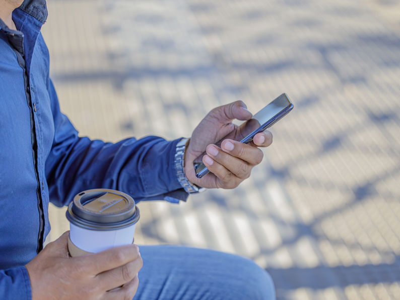 Detail Of The Hands Of A Man With A Mobile Phone And A Paper Cup Of Coffee