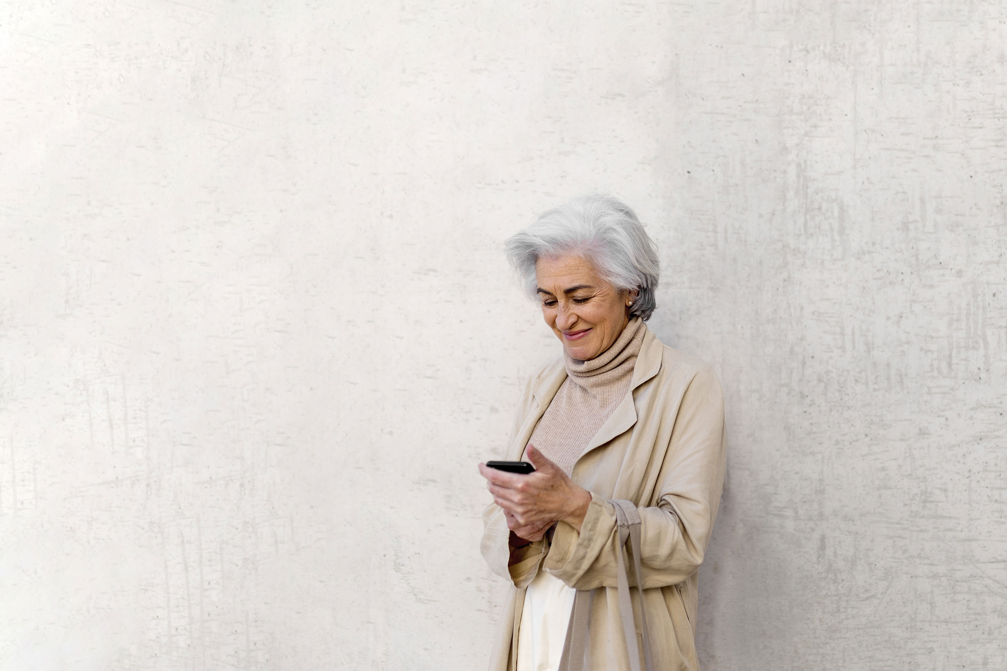Smiling Woman Using Mobile Phone In Front Of Wall