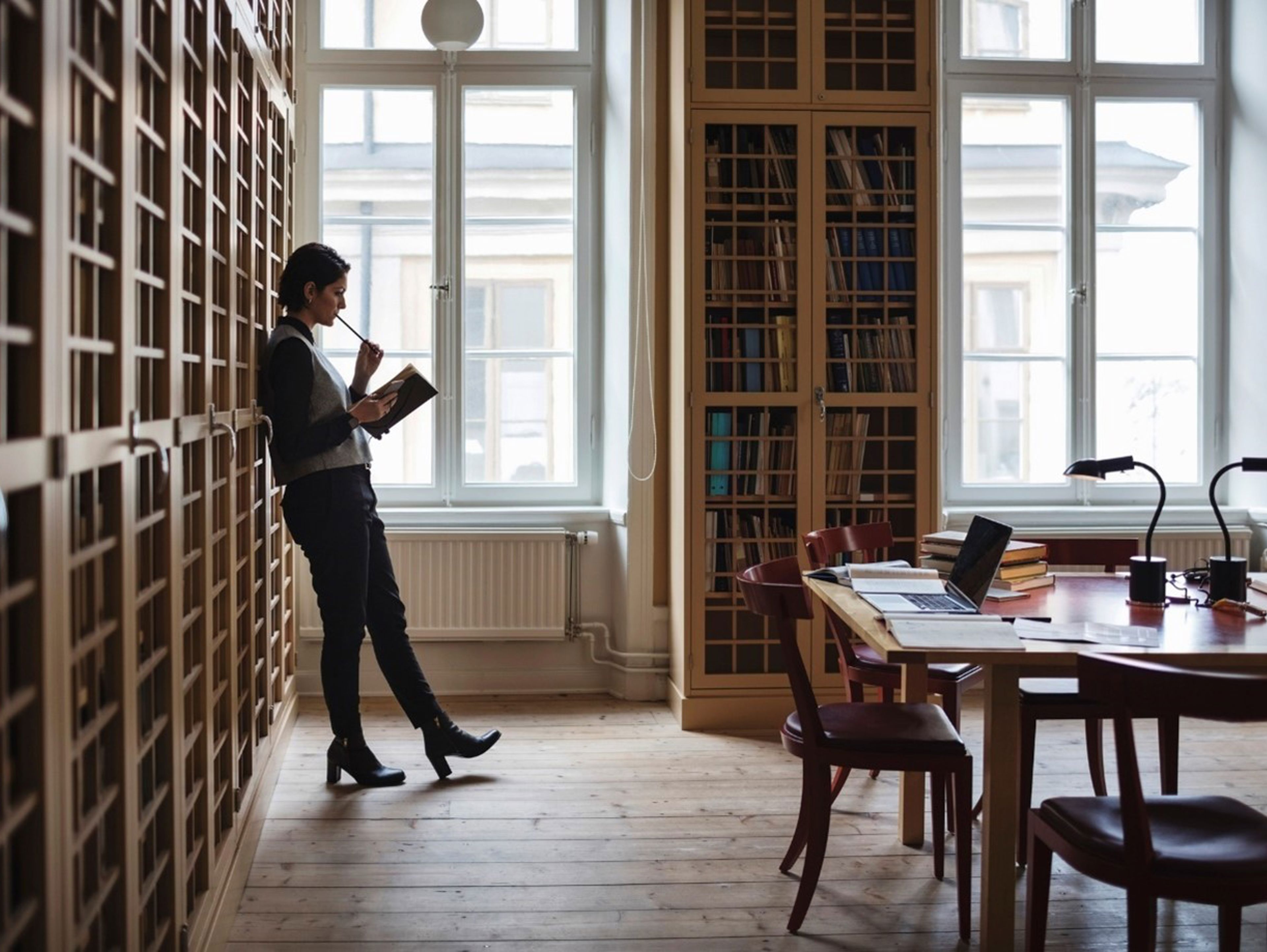 Women in library or study leaning against bookcase reading a book