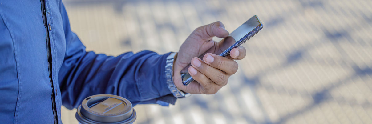 Detail Of The Hands Of A Man With A Mobile Phone And A Paper Cup Of Coffee