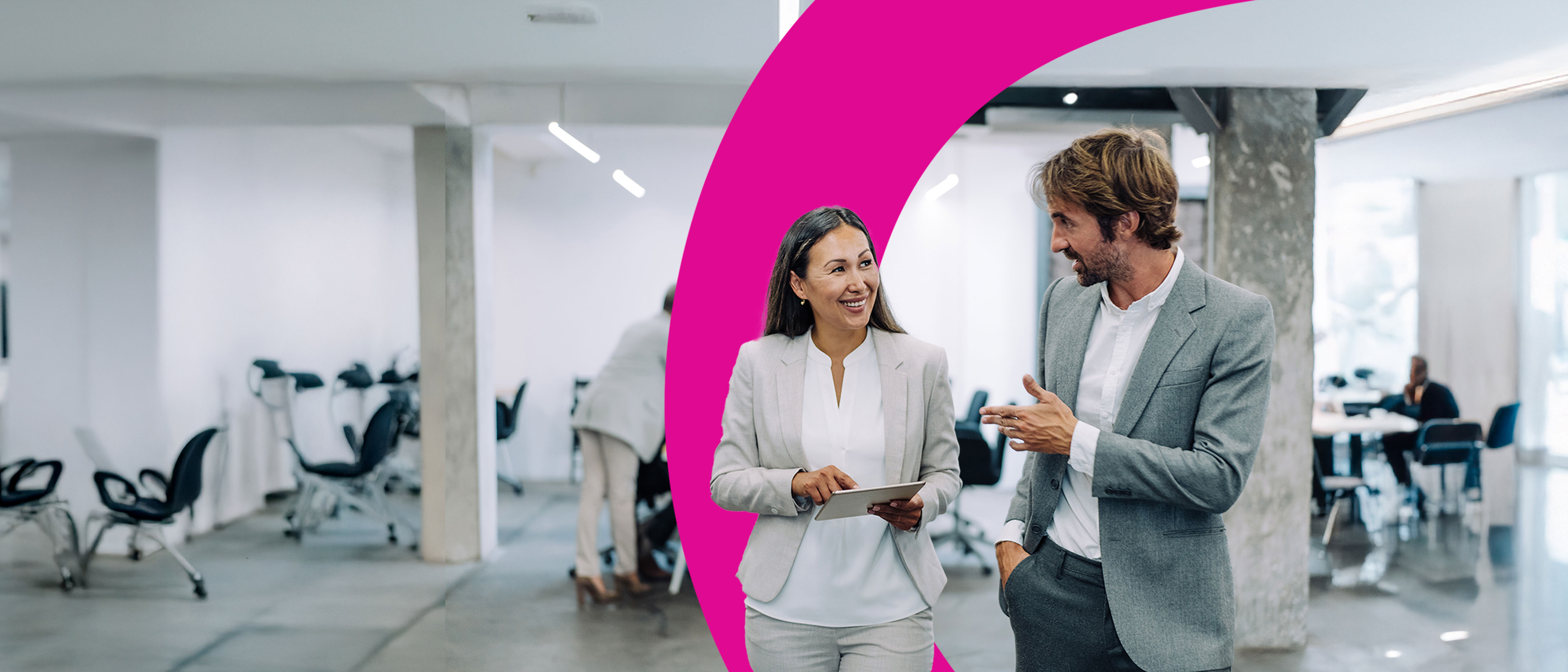 A woman in a suit stands at a podium, smiling and gesturing, while an audience sits in front of her. A projection screen displays a bar chart behind her in a bright, modern conference room.