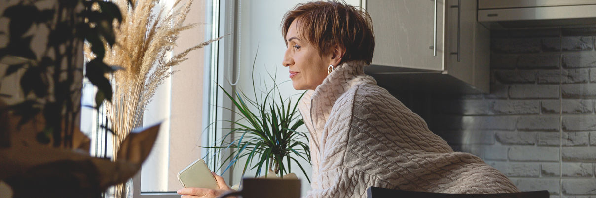 Woman In Beige Sweater Holds Phone And Looks Out Window