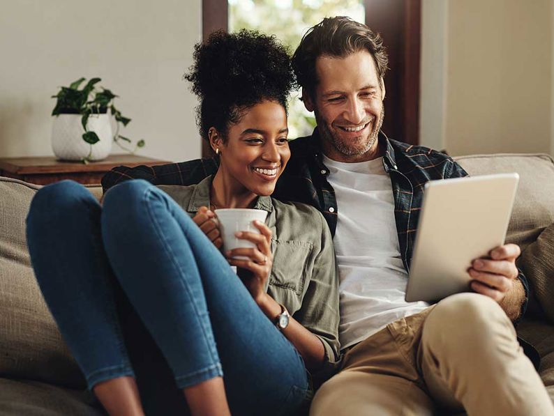 Couple on sofa holding tablet and cup