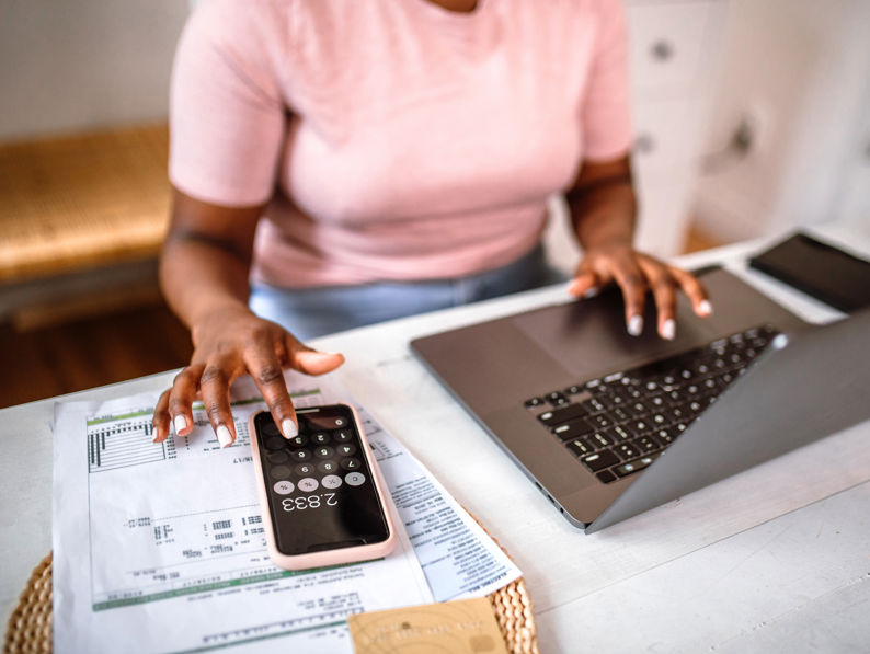 Women in pink top sitting at desk working on laptop of using calculator on her phone