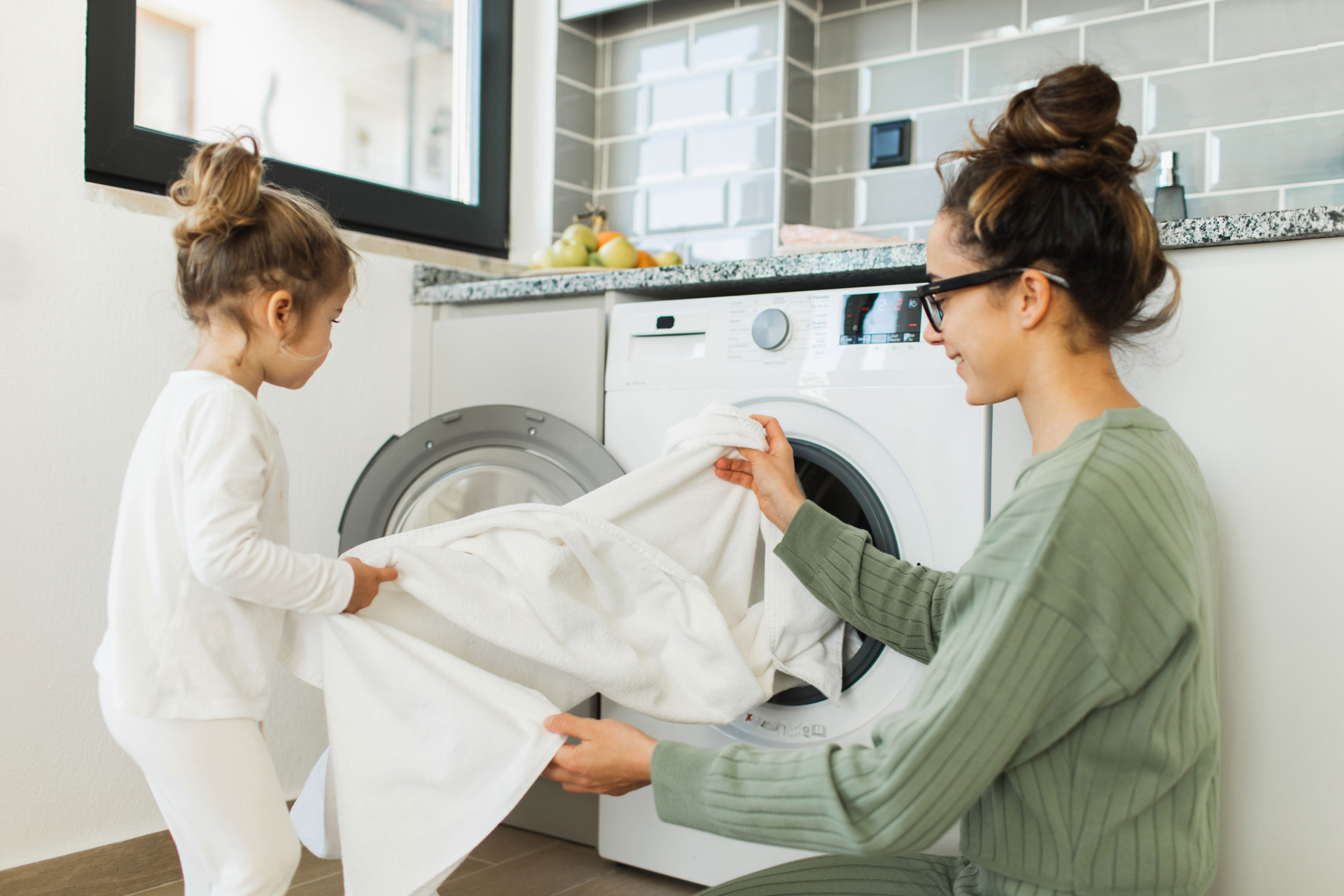 Mother and child girl little helper loading washing machine