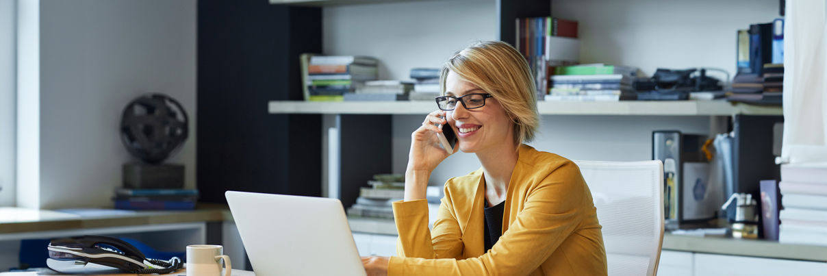 Businesswoman Using Laptop And Smart Phone At Desk