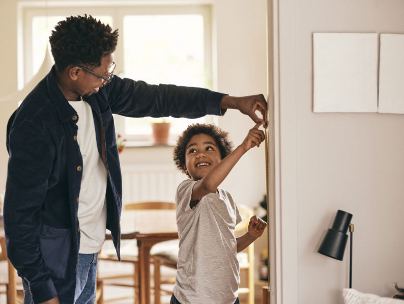 Smiling Son Looking At Father While Checking Height At Home