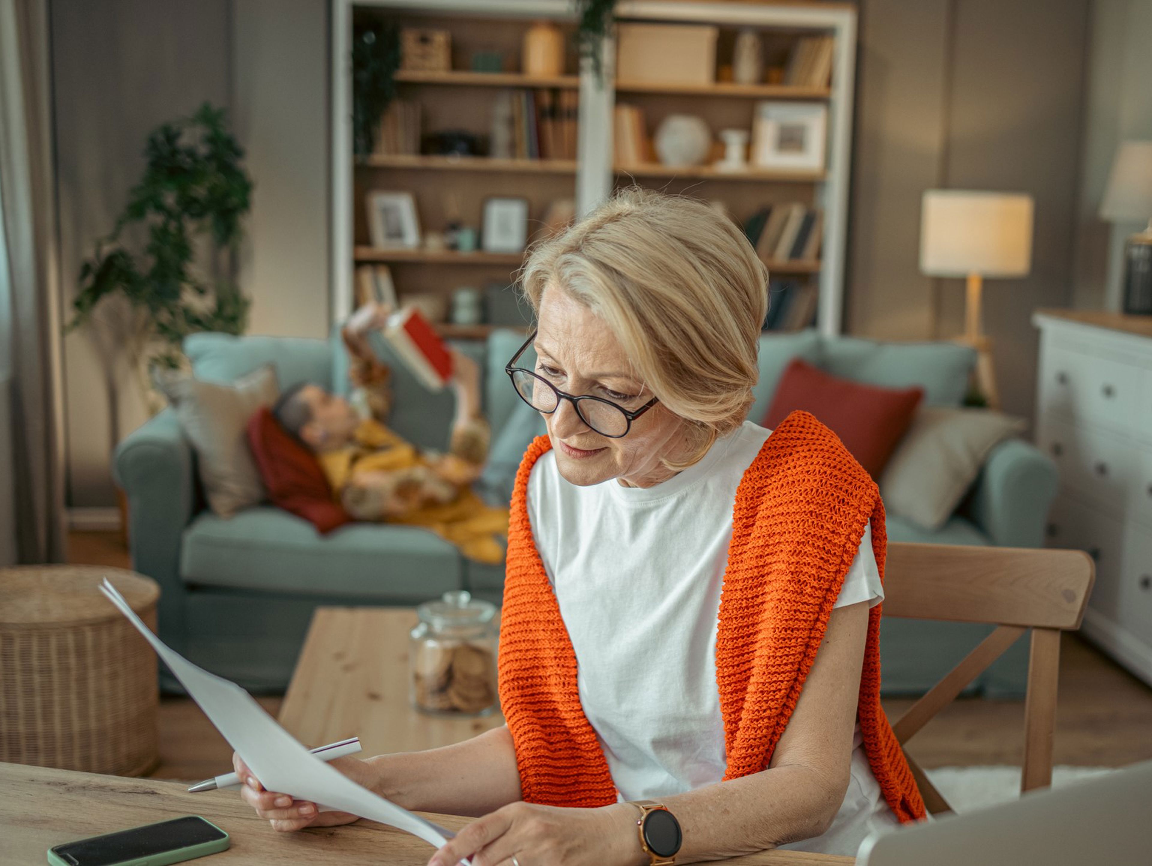Middle-aged women in bright orange jumper sitting at kitchen table working on a piece of paper