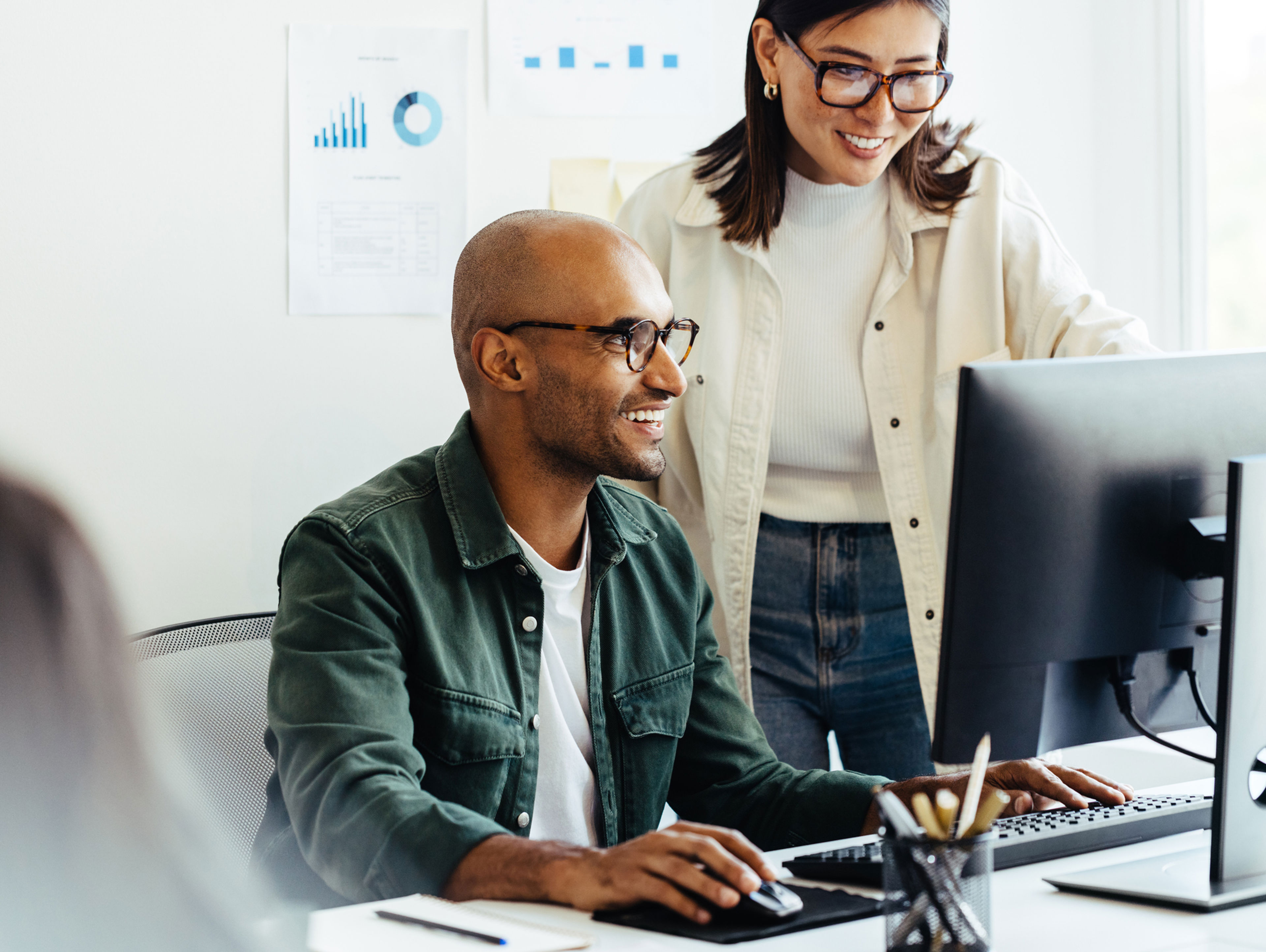 two co-workers huddled around desktop computer having a friendly conversation