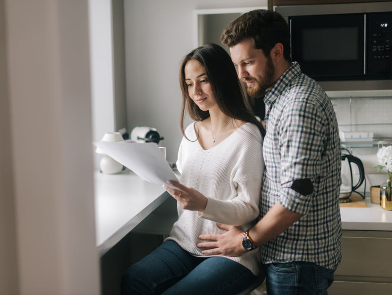 Smiling Young Couple Reading Documents At Home In The Kitchen