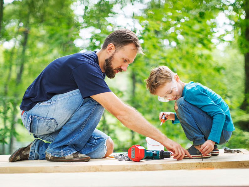 A person in a yellow raincoat stands on a rocky, misty shore looking out at the ocean, with grey clouds above and waves crashing against the rocks.