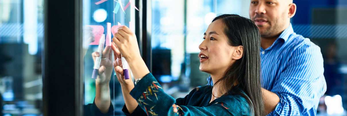 Businesswoman Sticking Notes On Glass With Colleague