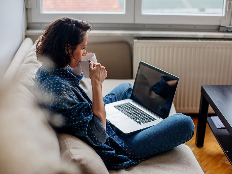 Lady Sat On Sofa With Laptop And White Mug