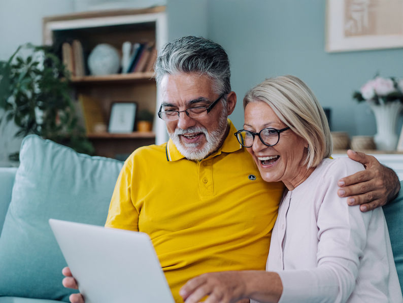 A man and woman sitting on a couch looking at a laptop.