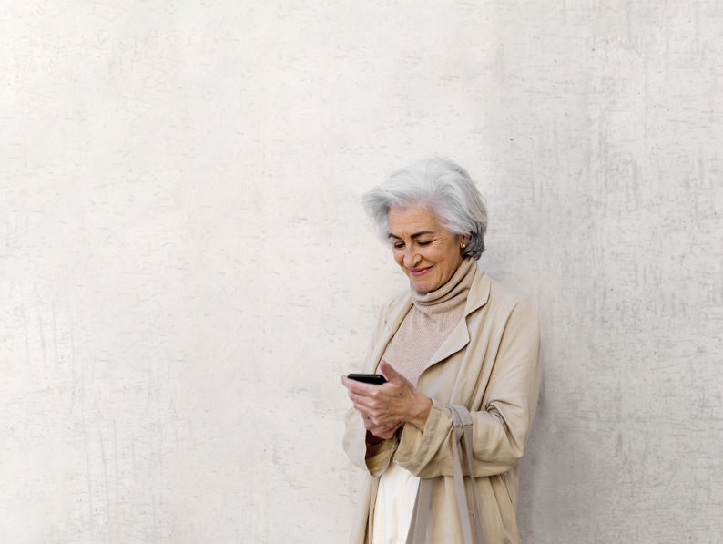 Smiling Woman Using Mobile Phone In Front Of Wall